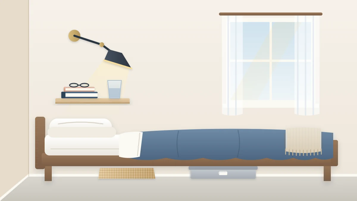 A bed close to a wall in a narrow room with a small floating wooden shelf beside the pillow holding a book and a glass, and a wall-mounted reading lamp above