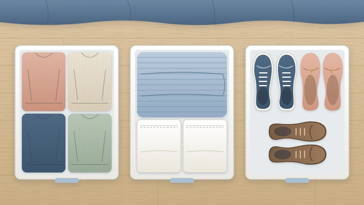 Top view of three open shallow under-bed boxes holding folded sweaters, a blanket with pillowcases and three pairs of shoes